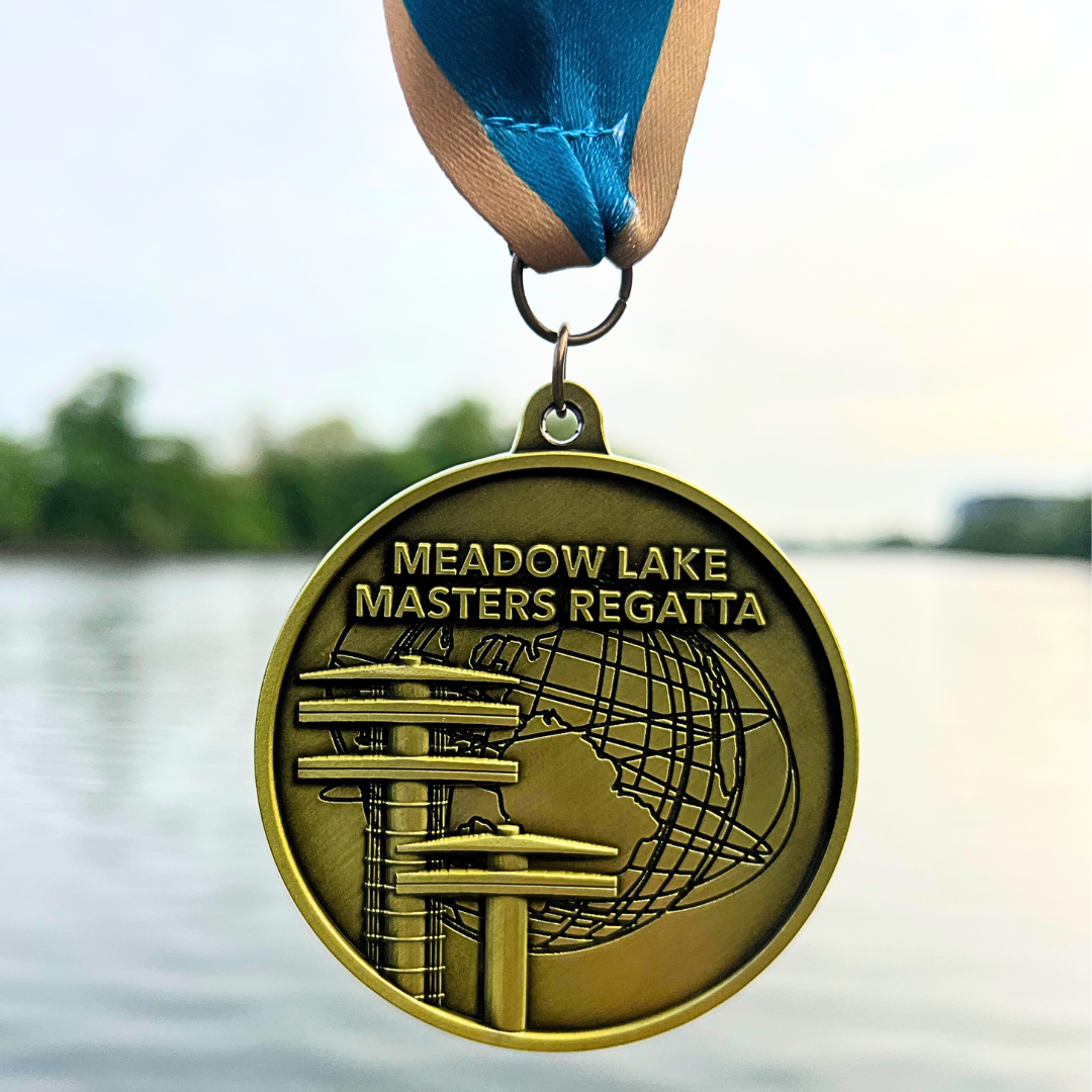 A medal is hanging on a ribbon and behind it is a body of water and trees in the background. The medal shows the Unisphere and two Observation Towers Flushing Meadows Corona Park. The medal says Meadow Lake Masters Regatta.